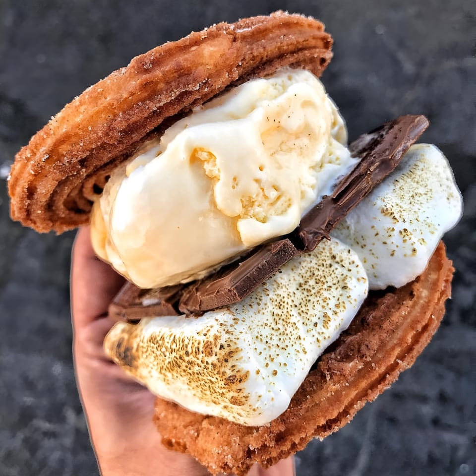 Hand holding a Churrito Loco s'mores churro sandwich with ice cream, toasted marshmallows, and chocolate.