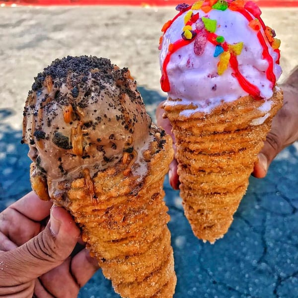 Two hands holding Churrito Loco churro cones with chocolate and strawberry ice cream, toppings, and drizzles.
