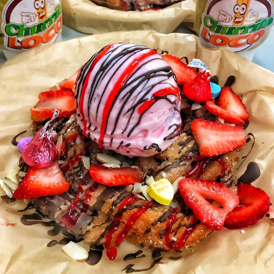 Churrito Loco dessert with churros, strawberries, ice cream, chocolate, and candy on brown paper.